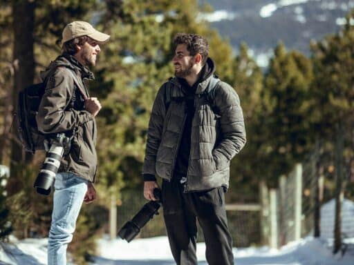 Positive men with cameras talking in winter forest