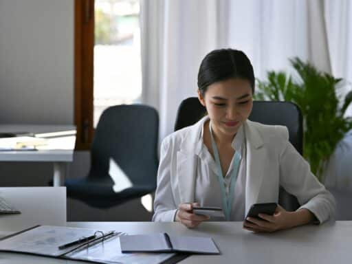 Smiling beautiful businesswoman holding credit card and shopping online with smart phone.